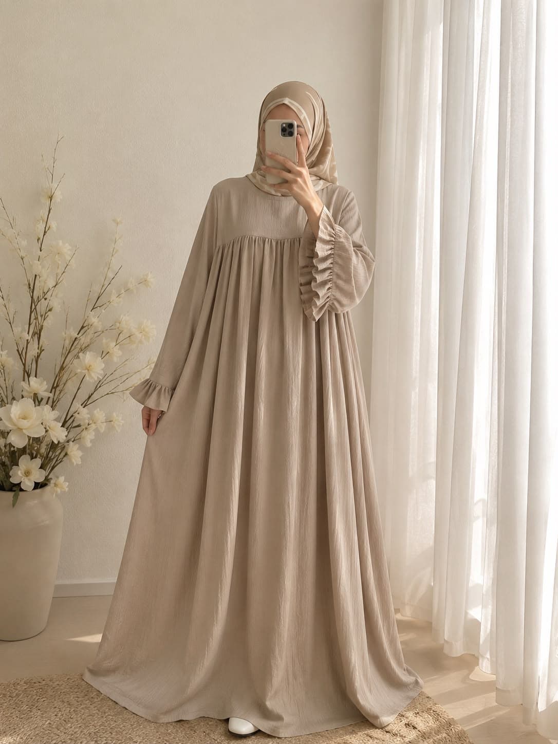 Full-length beige Abaya Elara with a gathered yoke and ruffled sleeve cuffs, worn with a patterned hijab