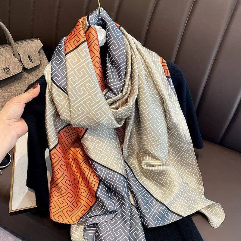 Silky scarf with a geometric orange, grey and cream print, draped over a chair